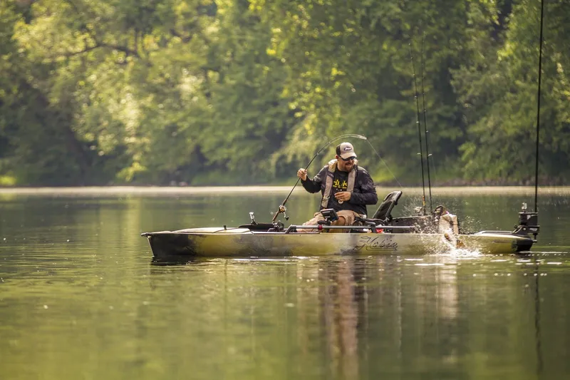 Slide: The Image of Man fishing on a 2022 Hobie MIRAGE PRO ANGLER 14 kayak in a serene lake. - 4