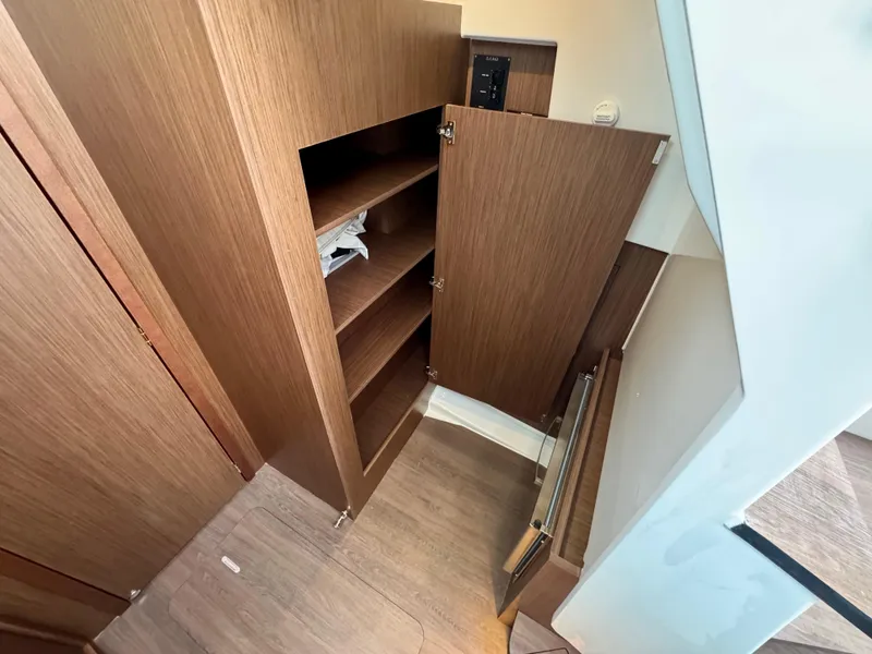 Slide: The Image of 2025 Beneteau Antares 11 interior with open wooden storage cabinets and stairs. - 24