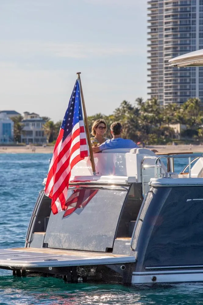 Slide: The Image of 2025 Sabre 58 Salon Express yacht with American flag, cruising near a coastal city. - 14