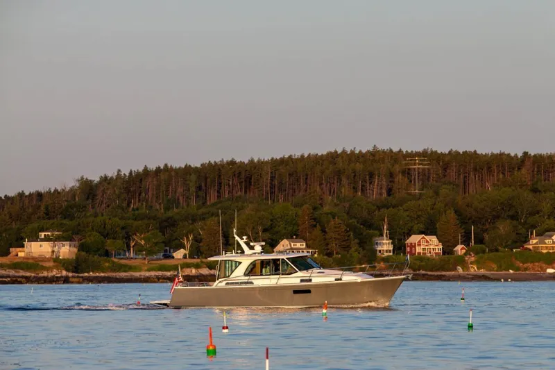 Slide: The Image of 2025 Sabre 43 Salon Express cruising on a serene lake with a forested shoreline. - 14