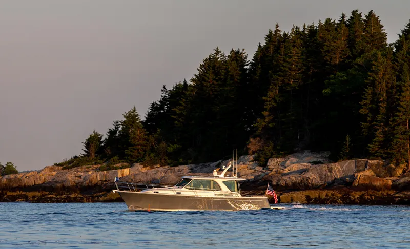 Slide: The Image of 2025 Sabre 43 Salon Express yacht cruising near a forested rocky shoreline. - 3