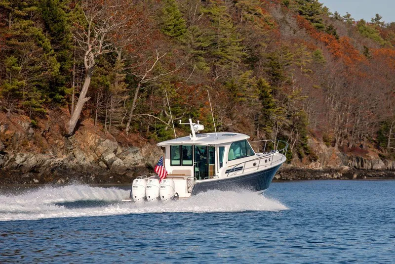 Slide: The Image of 2025 Back Cove 390 boat cruising on a scenic lake with forested shoreline. - 2