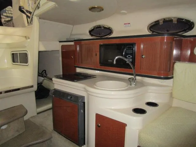 Slide: The Image of 2004 Sea Ray 260 Sundancer cabin with kitchenette, featuring sink, microwave, and storage cabinets. - 13