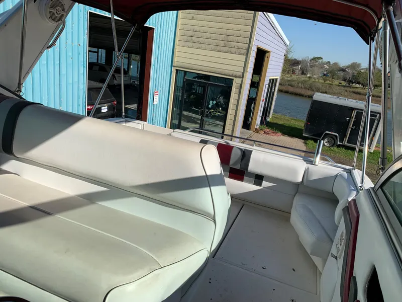 Slide: The Image of 1991 Sea Ray 290 Sundancer boat interior with seating, docked near blue and beige buildings. - 11