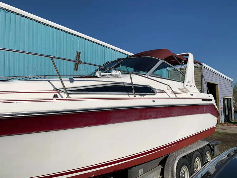 Slide: The Image of 1991 Sea Ray 290 Sundancer boat on trailer, red and white design, parked near blue building. - 26