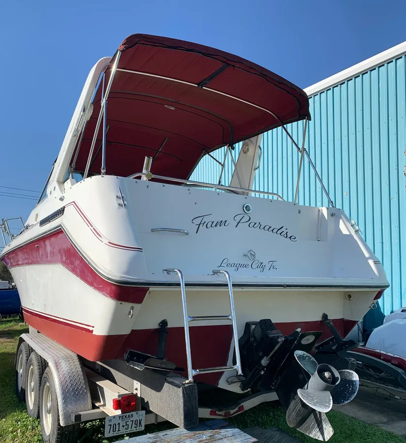 Slide: The Image of 1991 Sea Ray 290 Sundancer boat on trailer, red and white design, blue building background. - 31