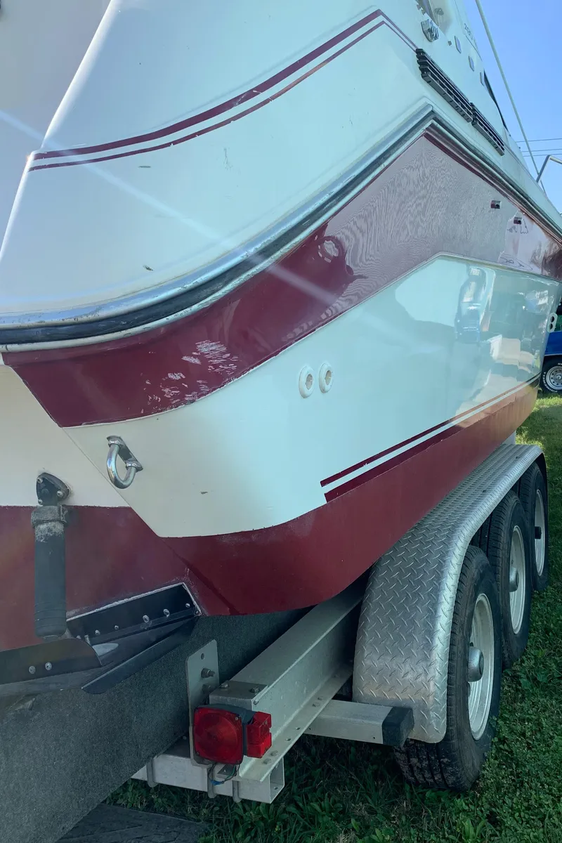Slide: The Image of 1991 Sea Ray 290 Sundancer boat on trailer, red and white hull, parked on grass. - 32