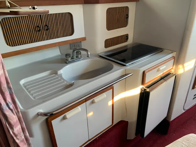 Slide: The Image of 1991 Sea Ray 290 Sundancer boat kitchen with sink, stove, and storage cabinets. - 9