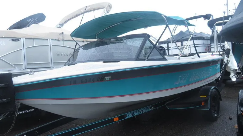 Slide: The Image of 1990 Nautique Ski boat with teal and white exterior, docked on a trailer. - 1