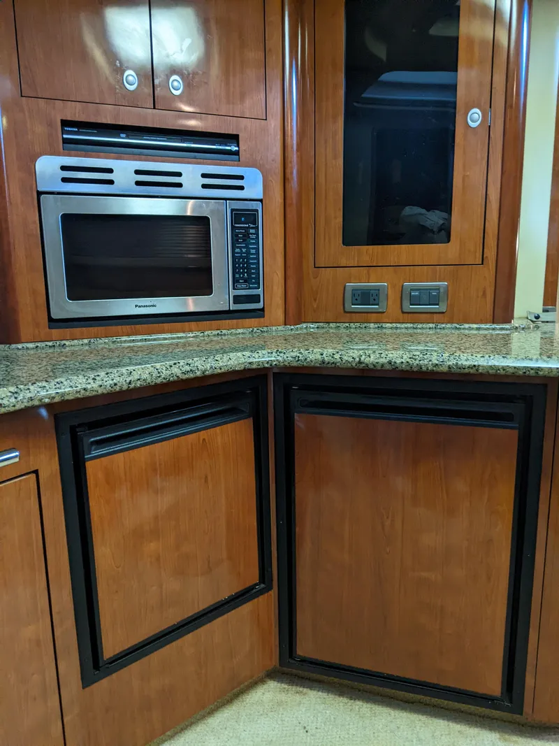 Slide: The Image of 2006 Sea Ray 44 Sundancer galley with microwave, granite countertop, and wooden cabinetry. - 21