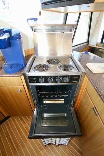Slide: The Image of 2002 Bayliner 3988 yacht kitchen with stove and oven, featuring wooden cabinetry and modern appliances. - 50