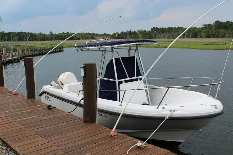 The Image of 1999 Boston Whaler Outrage 23 docked by a wooden pier on a calm lake. - 0
