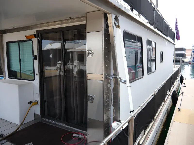 Slide: The Image of 1999 Custom 55x14 Stainless Houseboat docked, featuring sliding glass doors and exterior shower. - 10