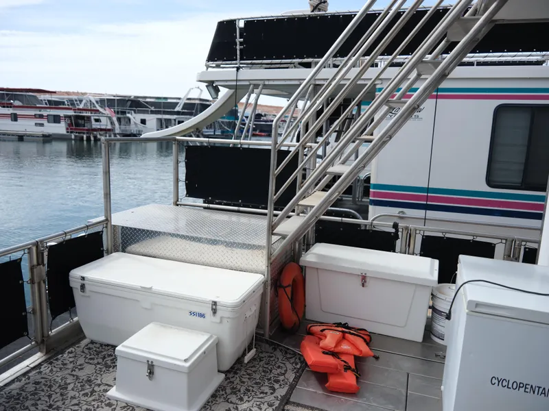 Slide: The Image of 1999 Custom 55x14 Stainless Houseboat deck with coolers, life jackets, and stairs. - 13