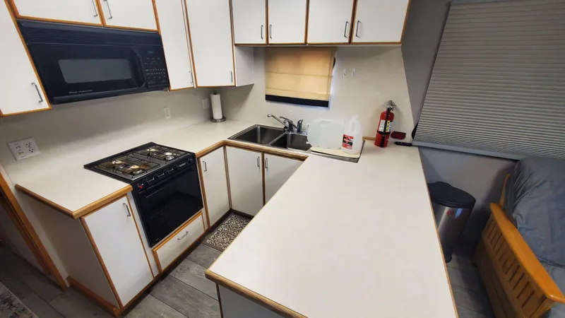 Slide: The Image of 1999 Custom 55x14 Stainless Houseboat kitchen with white cabinets, stove, microwave, and sink. - 5
