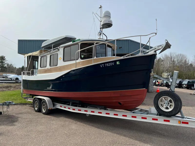 Slide: The Image of 2013 Ranger Tugs R-27 boat on trailer, blue and red hull, parked outdoors. - 10