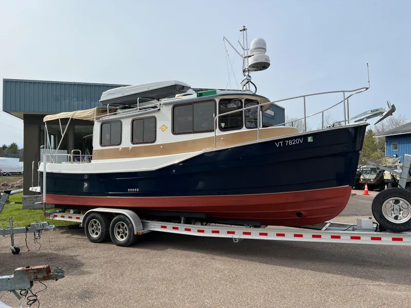 Slide: The Image of 2013 Ranger Tugs R-27 boat on trailer, blue and red hull, parked outdoors. - 11