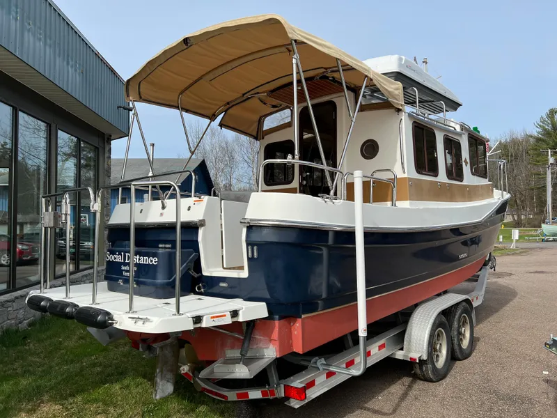 Slide: The Image of 2013 Ranger Tugs R-27 boat on trailer with canopy, parked near building. - 12