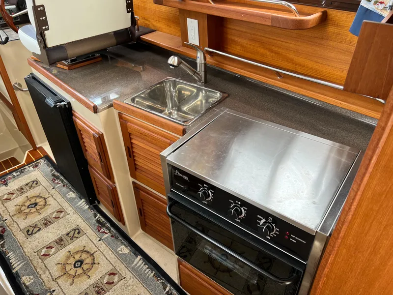 Slide: The Image of 2013 Ranger Tugs R-27 boat kitchen with sink, stove, and wooden cabinetry. - 44