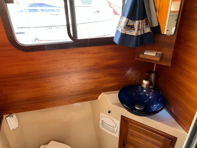 Slide: The Image of 2013 Ranger Tugs R-27 bathroom with wood paneling, blue sink, and nautical-themed curtain. - 50