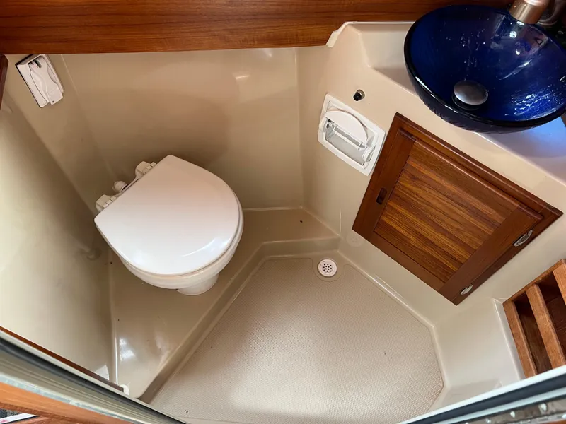 Slide: The Image of 2013 Ranger Tugs R-27 boat bathroom with toilet, wooden cabinet, and blue glass sink. - 51