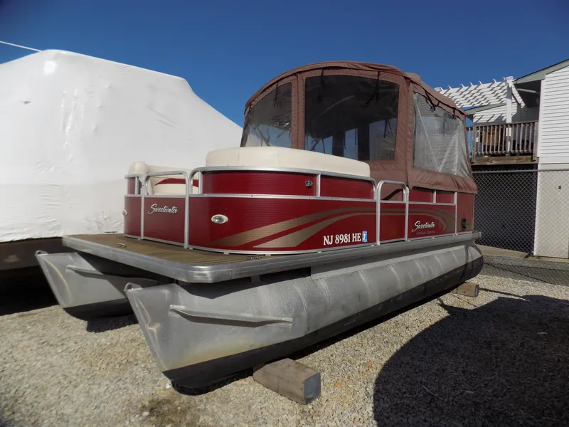 Slide: The Image of 2013 Sweetwater 2086 pontoon boat with red exterior, docked on gravel. - 0