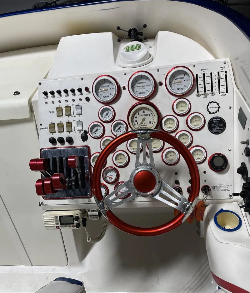 Slide: The Image of 1999 Fountain 47 Lightning boat dashboard with gauges, switches, and red steering wheel. - 12