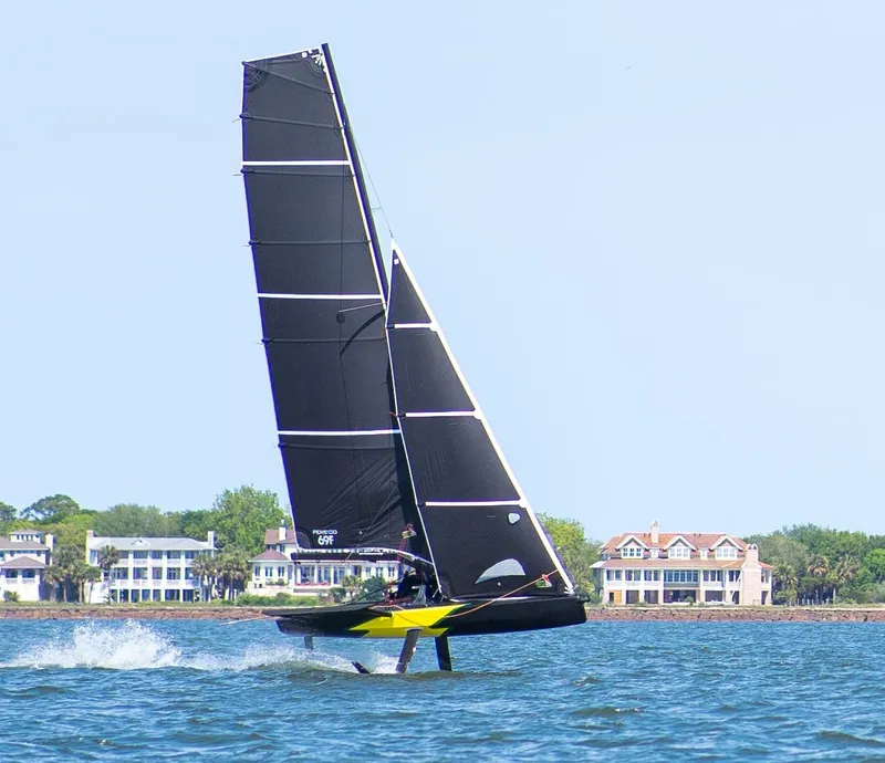 Slide: The Image of Sleek Persico 69F sailboat gliding on water, 2022 model, with coastal homes in background. - 1