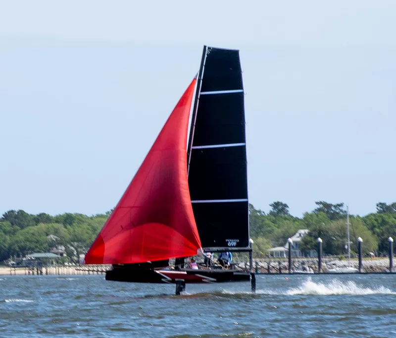 Slide: The Image of Sailing yacht Persico 69F 2022 with red sail gliding on water near shoreline. - 2