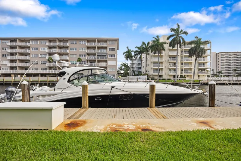 The Image of 2008 Sea Ray 44 Sundancer yacht docked near waterfront condos, under a clear blue sky. - 0