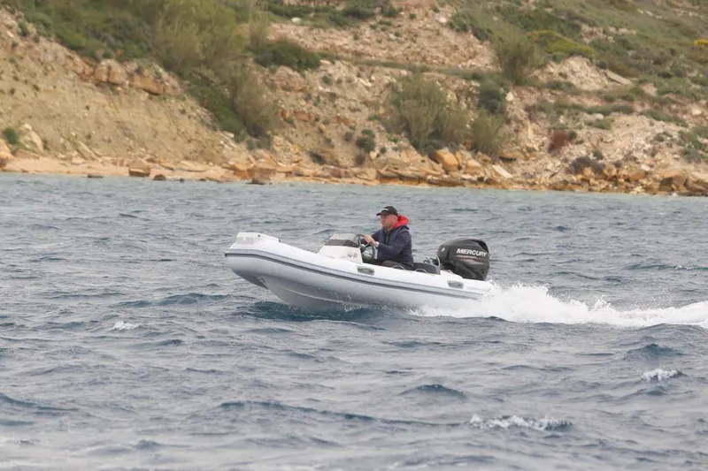 Slide: The Image of 2021 Northstar Axis 3.1 inflatable boat cruising on a choppy sea near rocky shoreline. - 3
