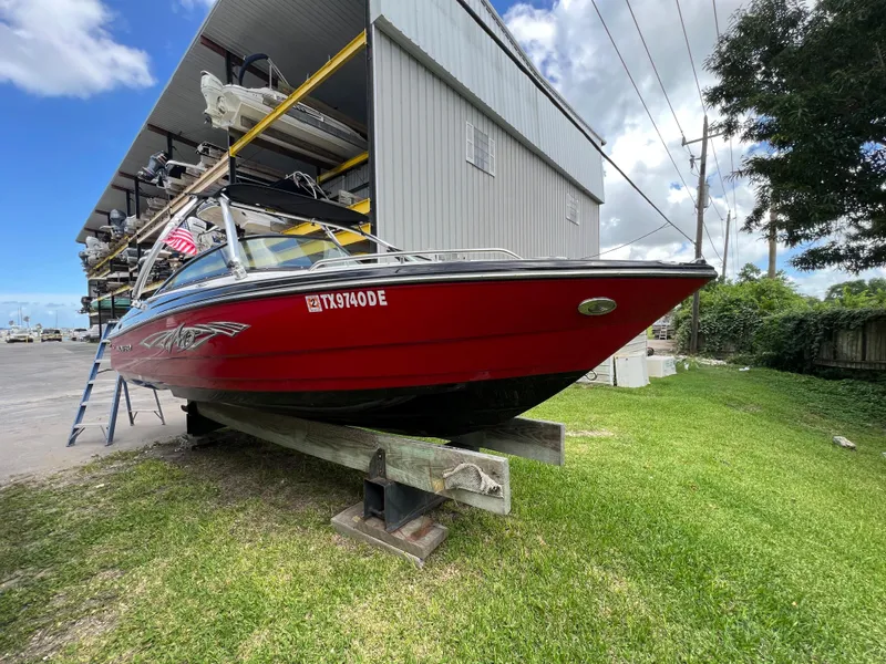 Slide: The Image of 2015 Monterey 224FSX boat in red, stored on a wooden stand near a storage facility. - 6