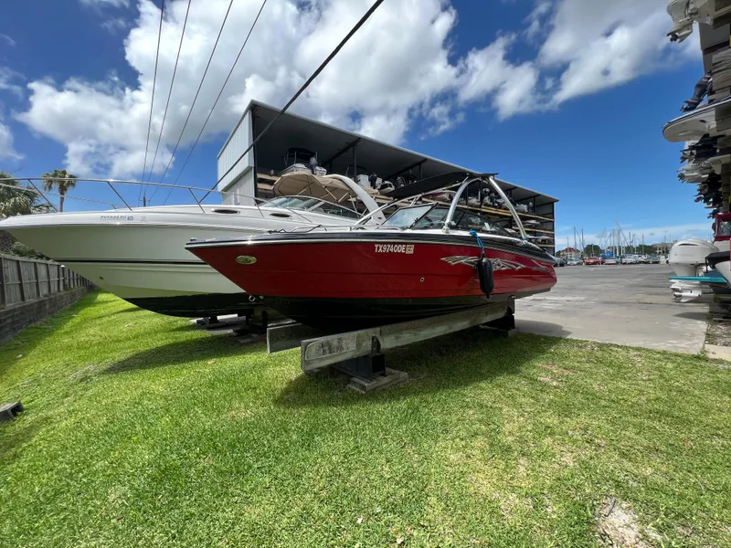 Slide: The Image of 2015 Monterey 224FSX boat in red, docked on grass near a marina. - 7