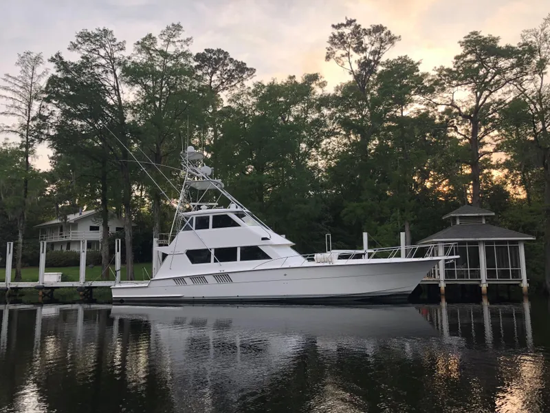 The Image of 1997 Hatteras 65 Convertible yacht docked by a serene, tree-lined waterfront. - 0
