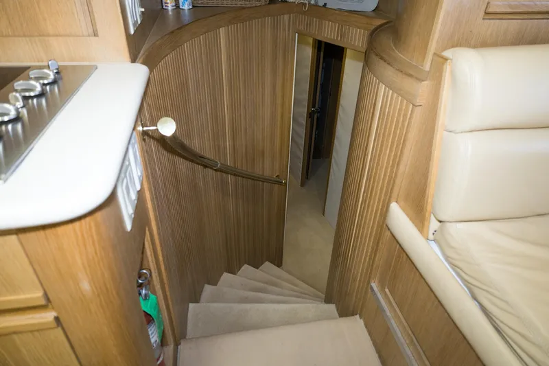Slide: The Image of Interior staircase of 1997 Hatteras 65 Convertible yacht, featuring wooden paneling and beige seating. - 14