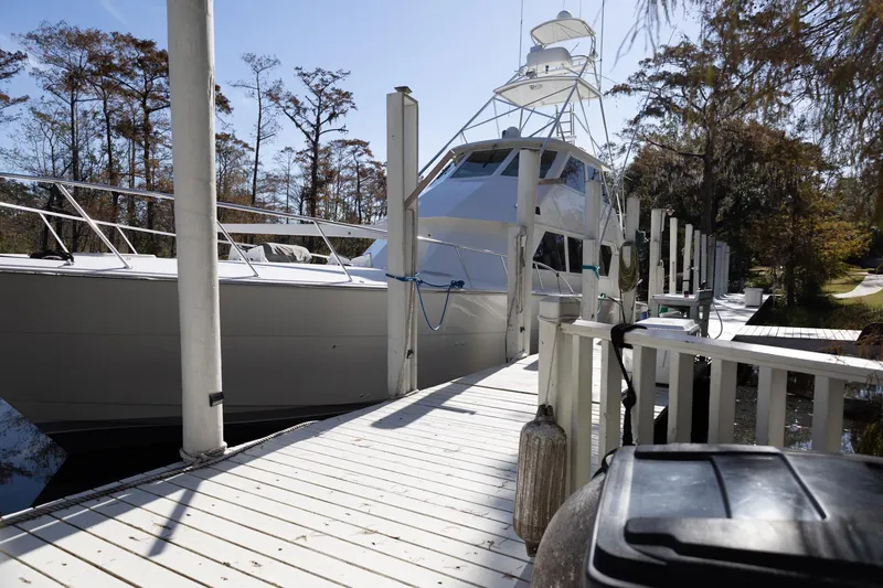 Slide: The Image of 1997 Hatteras 65 Convertible yacht docked at a marina with trees in the background. - 36