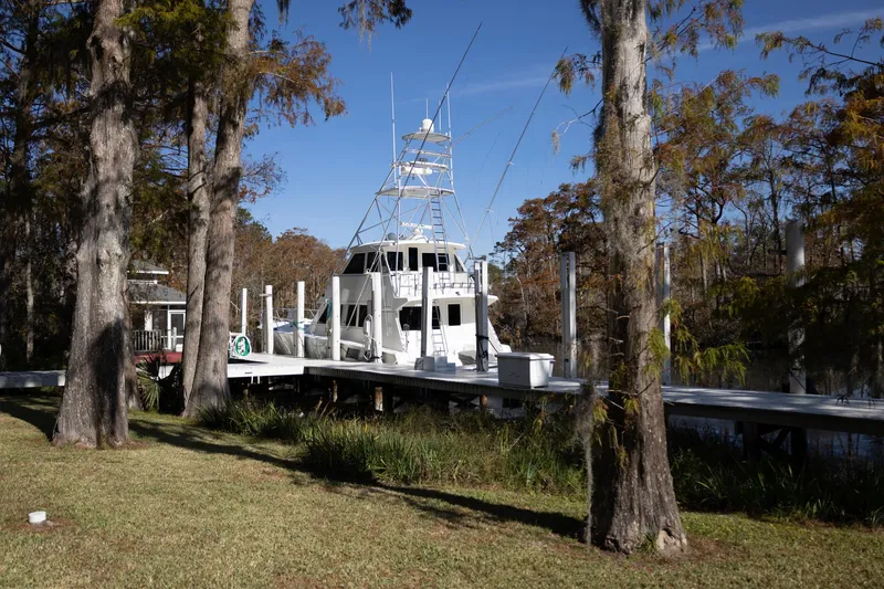 Slide: The Image of 1997 Hatteras 65 Convertible yacht docked by trees on a sunny day. - 38