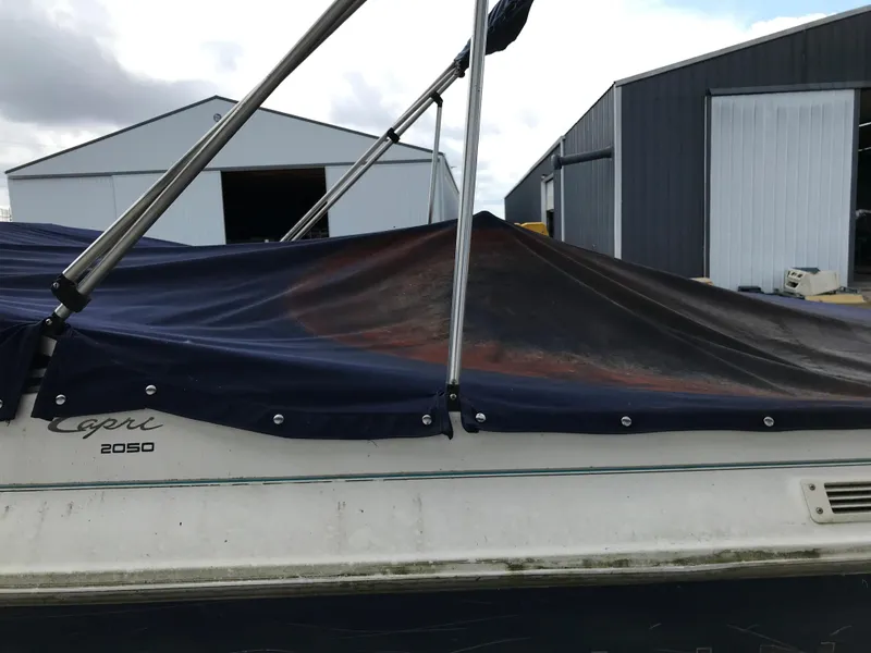 Slide: The Image of 1997 Bayliner 2050 Capri boat with a blue cover, parked near storage sheds. - 6