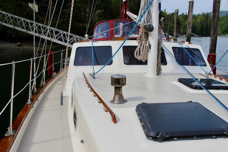 Slide: The Image of 1981 Skookum 53 sailboat deck with ropes and hatches, docked near lush greenery. - 22