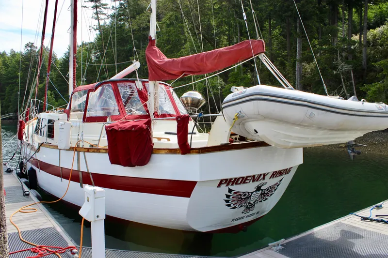 Slide: The Image of 1981 Skookum 53 sailboat docked with dinghy, surrounded by lush forest. - 8