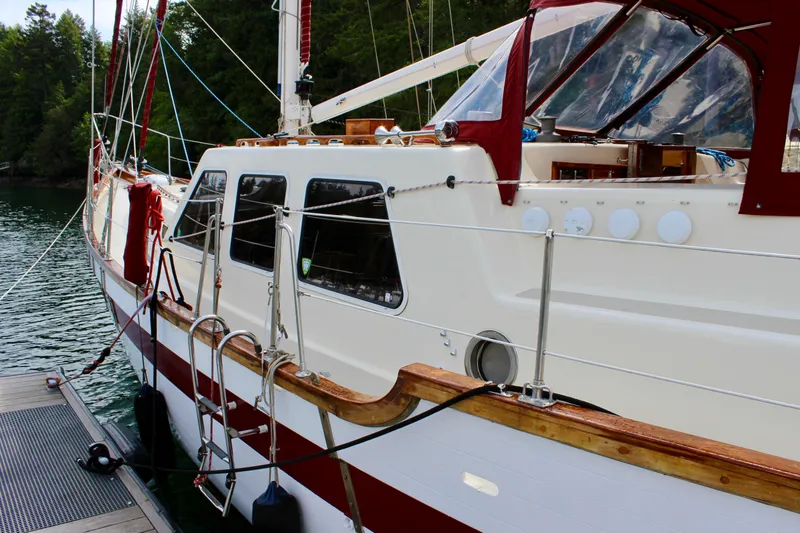 Slide: The Image of 1981 Skookum 53 sailboat docked, featuring red and white design with lush forest backdrop. - 9
