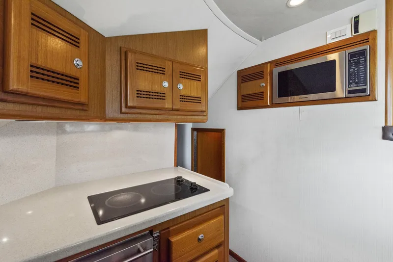 Slide: The Image of 2002 Cabo Convertible Painted yacht kitchen with stove, microwave, and wooden cabinets. - 27