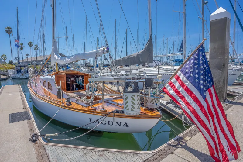 Slide: The Image of 1950 Custom Cornu Sloop Laguna docked with American flag, marina background. - 1