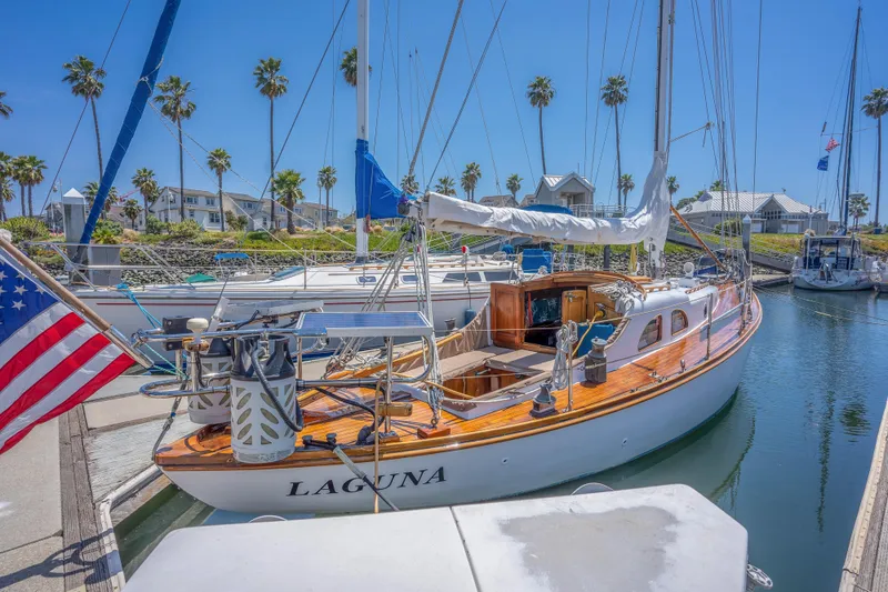 Slide: The Image of 1950 Custom Cornu Sloop sailboat Laguna docked at a marina with palm trees. - 2
