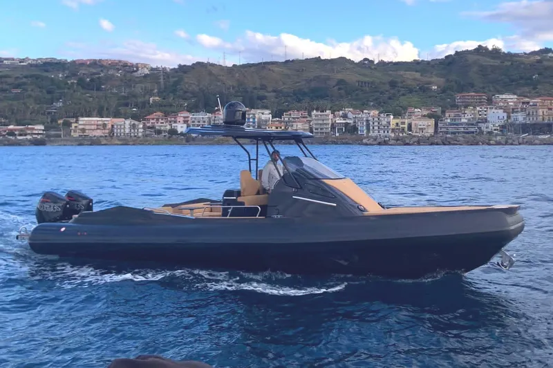 Slide: The Image of 2025 SPX RIB 38 Sport boat cruising on water near coastal town. - 13