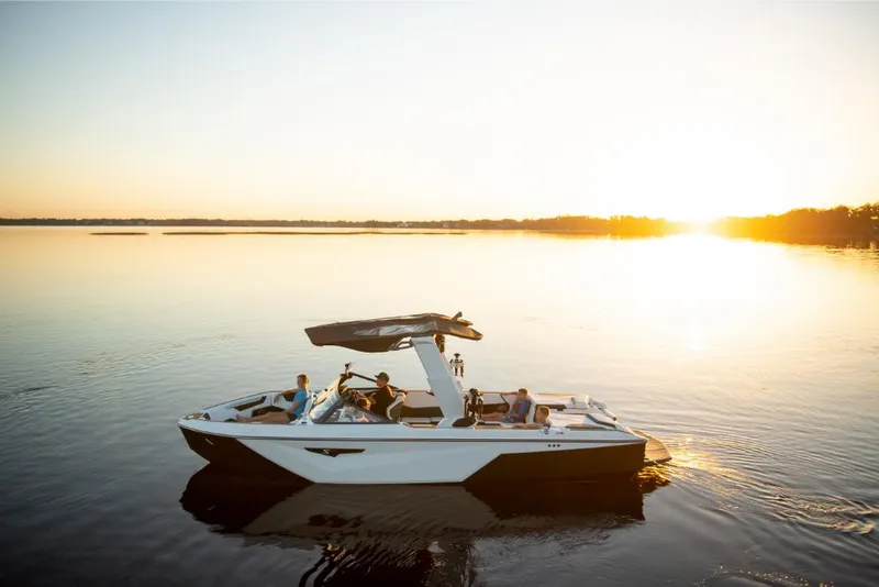 Slide: The Image of 2023 Nautique Super Air Nautique S25 boat on a serene lake at sunset. - 11