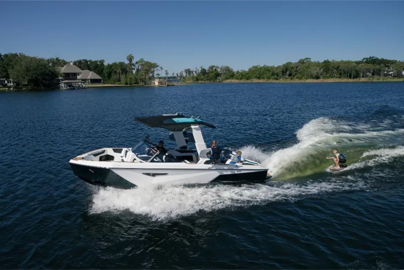 Slide: The Image of 2023 Nautique Super Air Nautique S25 towing a wakeboarder on a serene lake. - 17