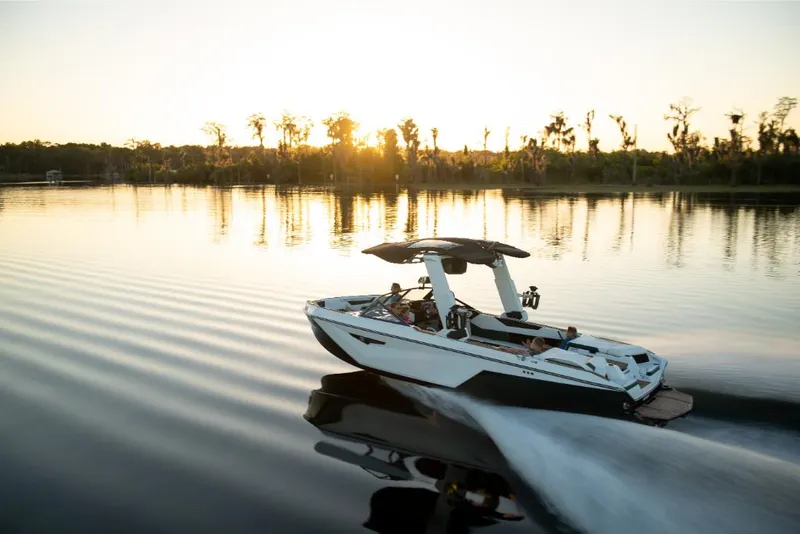 Slide: The Image of 2023 Nautique Super Air Nautique S25 boat cruising on a serene lake at sunset. - 34