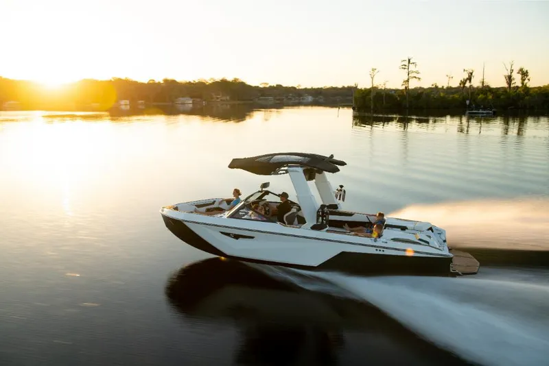 Slide: The Image of 2023 Nautique Super Air Nautique S25 boat cruising on a serene lake at sunset. - 35