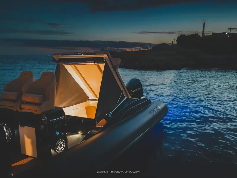 Slide: The Image of 2025 SPX RIB 32 Dinette boat illuminated at dusk on calm waters. - 15